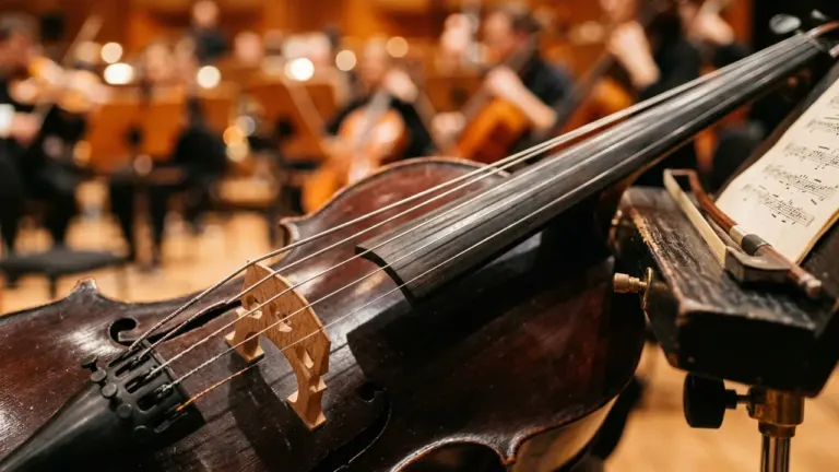 Gros plan sur un violoncelle en bois avec son archet et partition dans un orchestre.