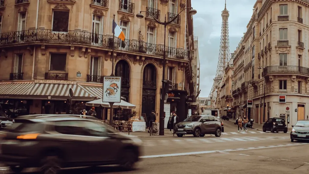 Voitures circulant dans une rue parisienne bordée d'immeubles haussmanniens classiques.