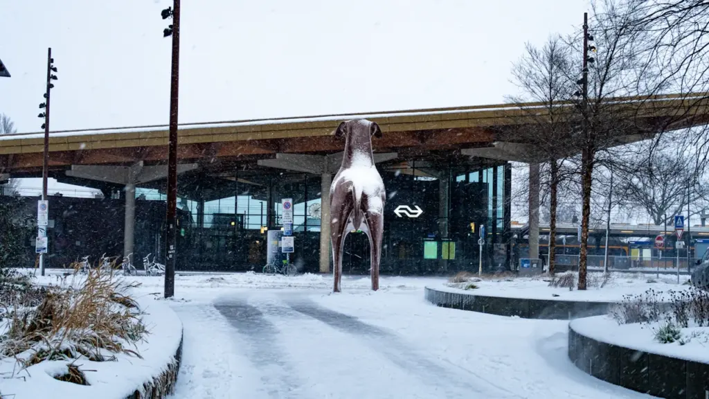 Une statue de chien devant une gare sous la neige en hiver.