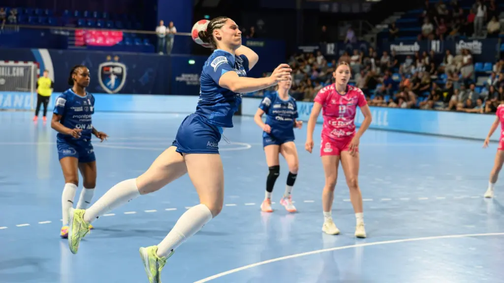 Une joueuse de handball en plein saut s'apprête à tirer le ballon vers le but.