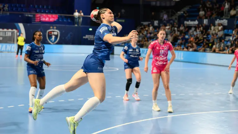 Une joueuse de handball en plein saut s'apprête à tirer le ballon vers le but.
