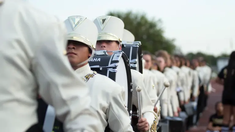 Membres d'une fanfare en uniforme blanc alignés lors d'une cérémonie en extérieur.