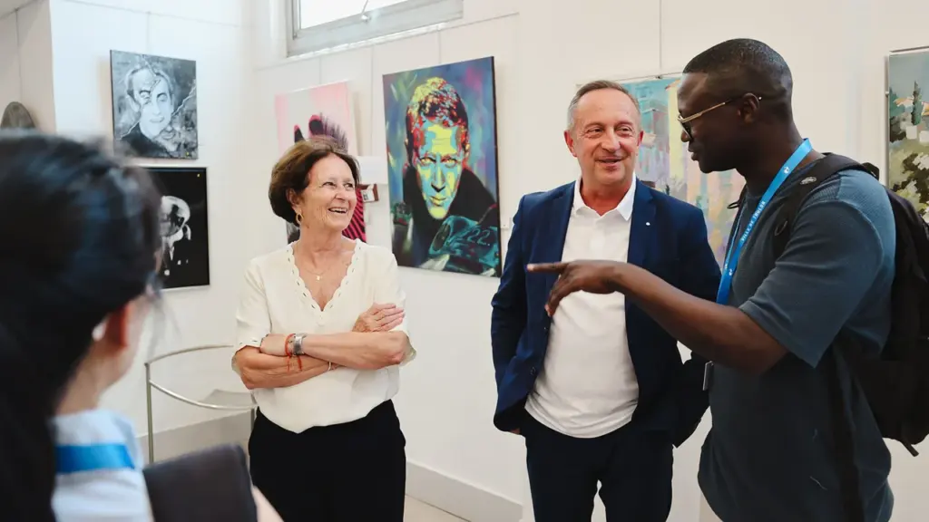 Trois personnes discutent joyeusement dans une galerie d'art devant des tableaux colorés aux murs.