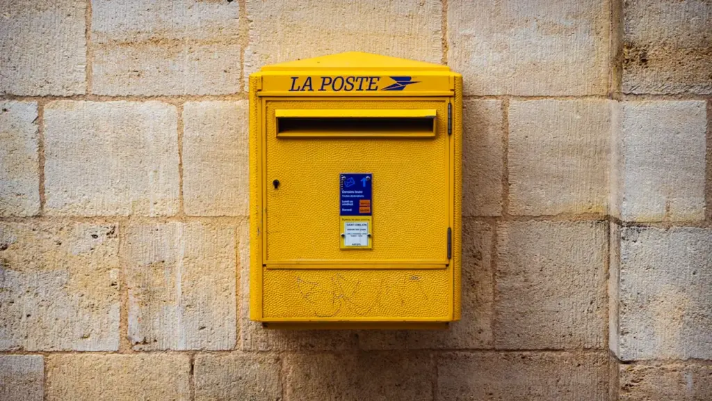 Une boîte aux lettres jaune emblématique de La Poste sur un mur en pierre.