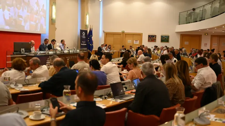 Une assemblée nombreuse assiste à une réunion formelle dans une salle de conférence municipale.