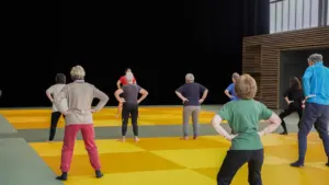 Un groupe de seniors effectue des exercices de fitness sur un tapis de sol jaune.
