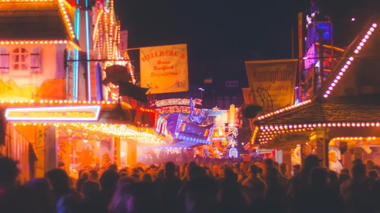 Ambiance nocturne animée d'une fête foraine avec des illuminations colorées et une foule.