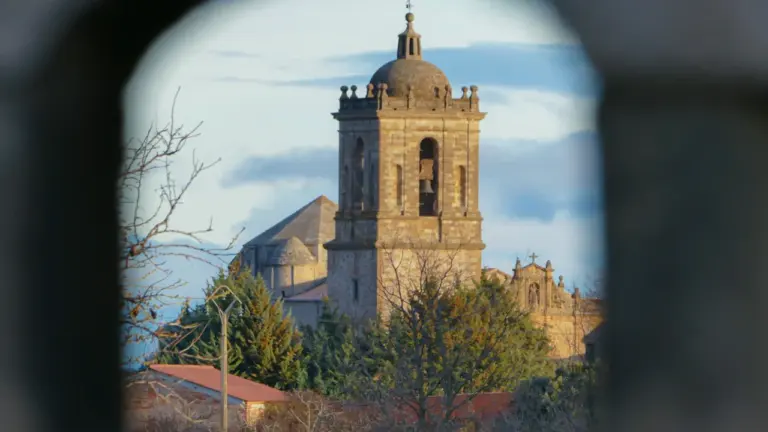 Vue encadrée d'un clocher en pierre ancienne sous un ciel ensoleillé.