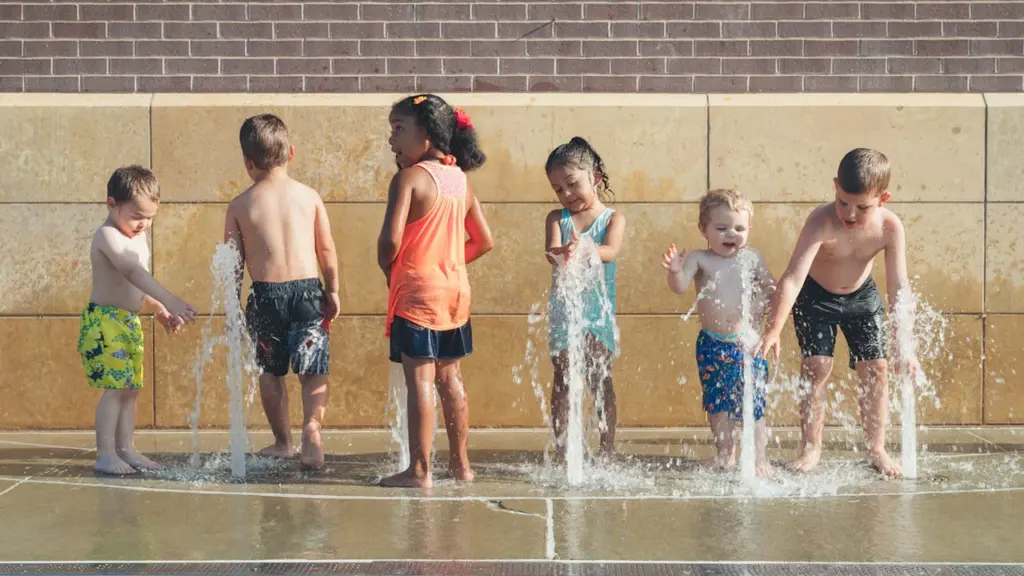 Un groupe d'enfants jouant avec des jets d'eau dans un parc public estival.