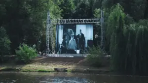 Un grand écran de cinéma installé en extérieur dans un parc verdoyant au bord de l'eau.