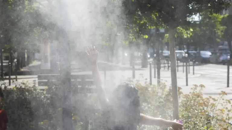 Une personne vue de dos lève les bras dans un nuage de brumisateur extérieur.