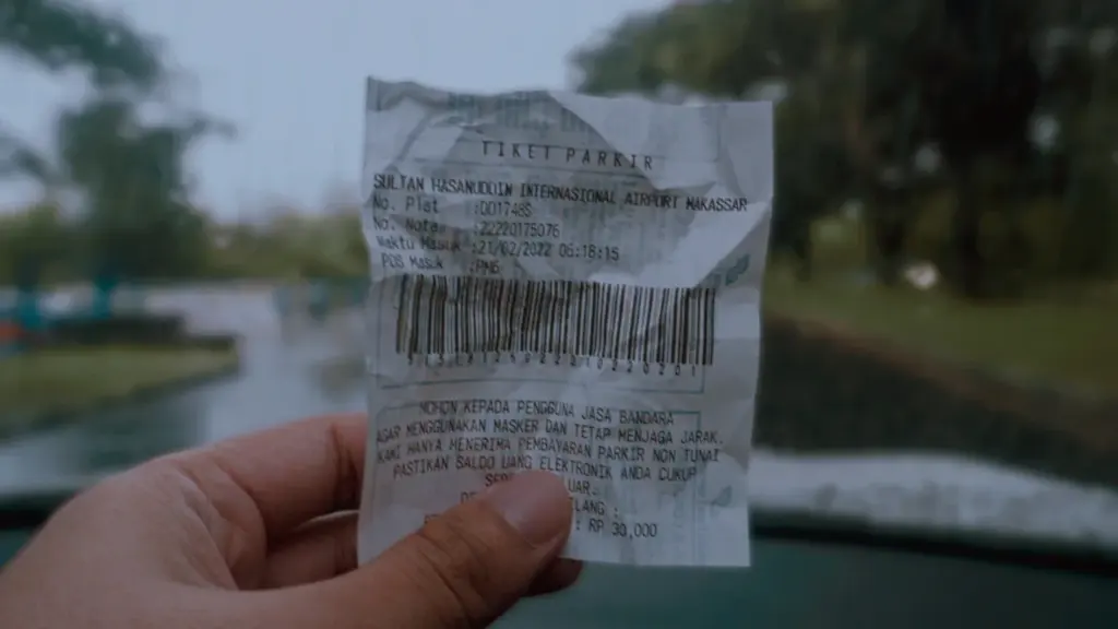 Main en tenant un ticket de stationnement imprimé avec un code-barres bien visible.