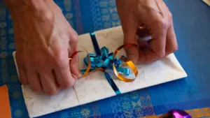Mains préparant un paquet cadeau soigneusement décoré avec un ruban bleu.