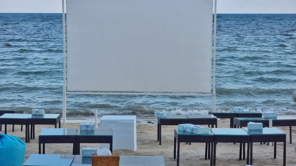 Un écran de cinéma en plein air installé sur une plage au coucher du soleil.