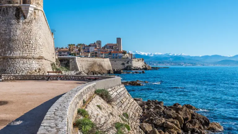Vue panoramique du vieux Antibes et des Alpes enneigées en arrière-plan en bord de mer.