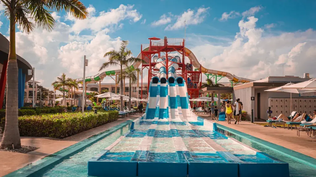 Grand parc aquatique extérieur avec toboggans colorés et palmiers sous un ciel bleu.