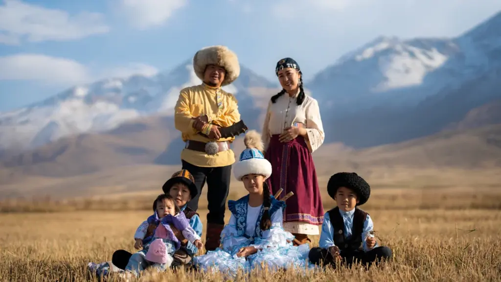 Une famille en costumes traditionnels posant dans un champ devant des montagnes enneigées.