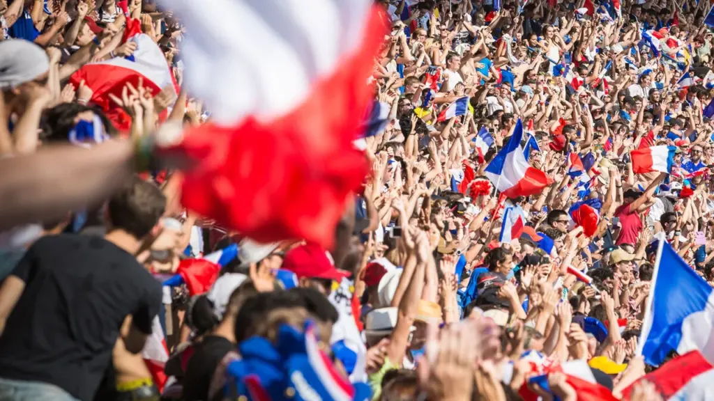 Une foule nombreuse agite fièrement des drapeaux français lors d'un événement sportif en extérieur.