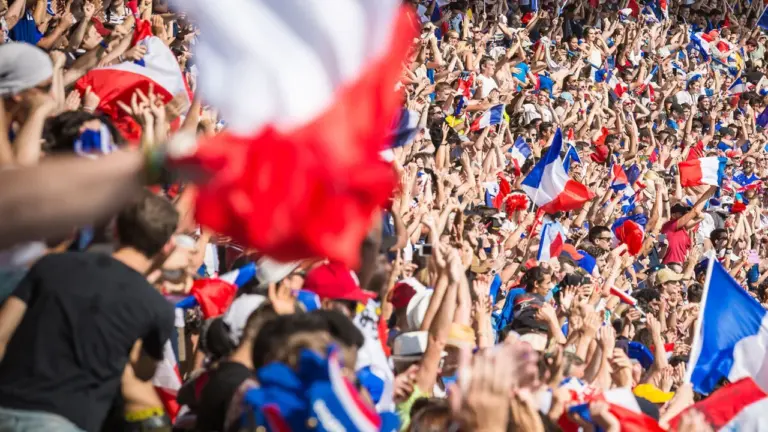 Une foule nombreuse agite fièrement des drapeaux français lors d'un événement sportif en extérieur.