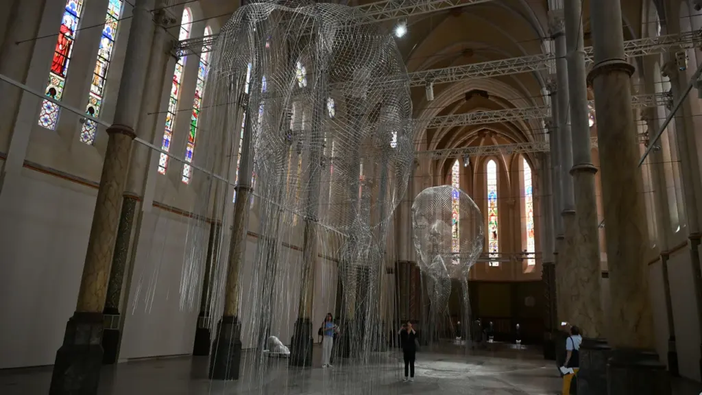 Deux sculptures en grillage métallique suspendues dans la nef d'une église aux vitraux colorés.