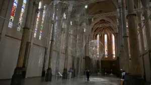 Deux sculptures en grillage métallique suspendues dans la nef d'une église aux vitraux colorés.