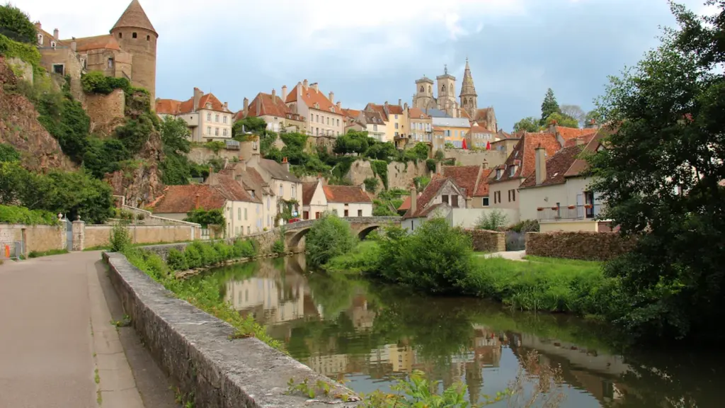 Vue pittoresque d'un village français avec une rivière et une architecture historique.
