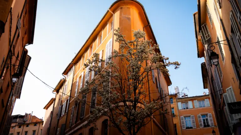 Immeuble aixois traditionnel avec une façade ocre dans une rue étroite et ensoleillée.