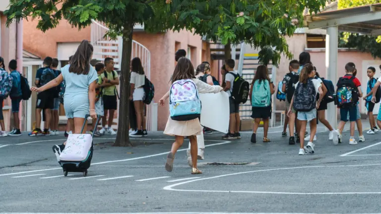 De nombreux élèves avec leurs sacs à dos traversent une cour d'école en extérieur.