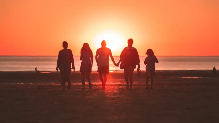 Une famille marchant sur une plage au coucher du soleil en été.