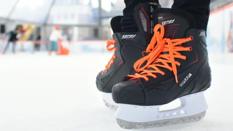 Gros plan sur des patins à glace noirs portés par un enfant sur une patinoire.