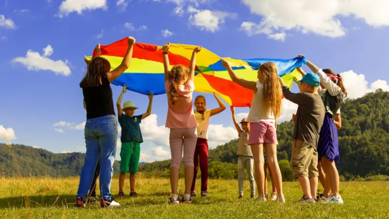 Un groupe d'enfants joue avec un parachute coloré dans une prairie ensoleillée.