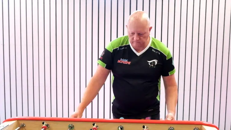Un joueur de baby-foot chauve en maillot noir et vert concentré sur le match.