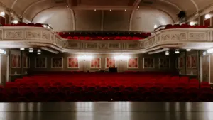 Vue intérieure d'un théâtre classique avec des rangées de sièges rouges.