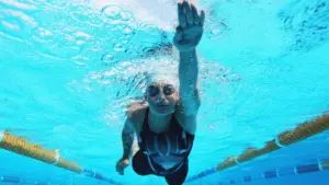 Une nageuse porte des lunettes de protection et nage en crawl dans une piscine olympique.