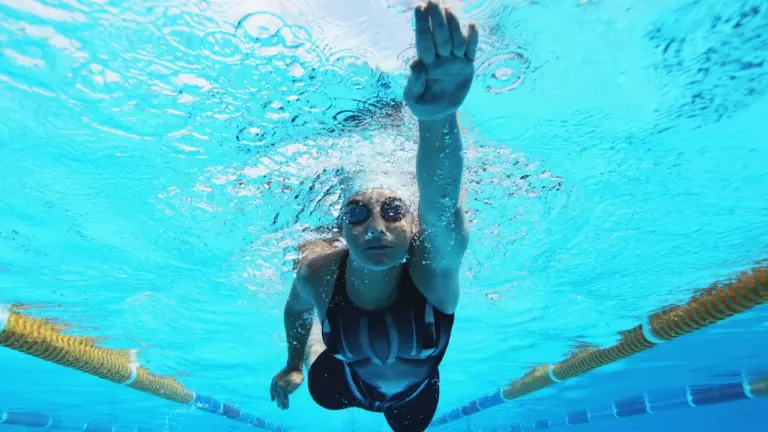 Une nageuse porte des lunettes de protection et nage en crawl dans une piscine olympique.