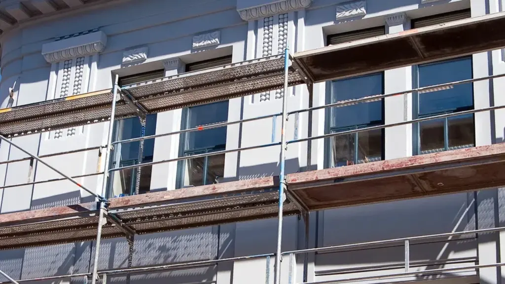 Échafaudage métallique installé devant la façade grise d'un immeuble historique en cours de rénovation.