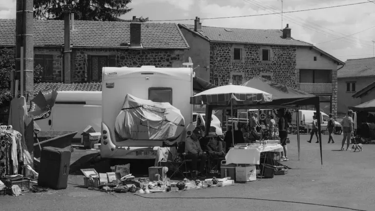 Un étal de vide-grenier extérieur avec des objets divers sous un parasol.