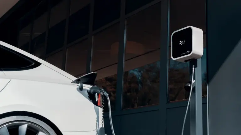 Une voiture électrique blanche est branchée à une borne de recharge moderne en extérieur.
