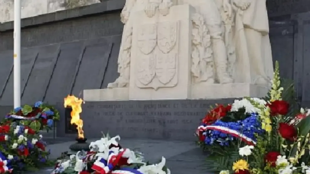 Monument aux morts en pierre entouré de couronnes de fleurs tricolores avec flamme allumée.