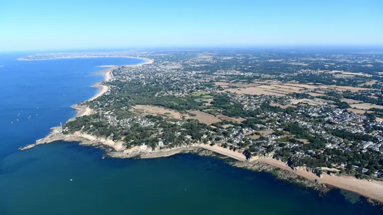 Vue aérienne d'une côte française avec plages, falaises rocheuses et zones résidentielles entourées d'arbres.