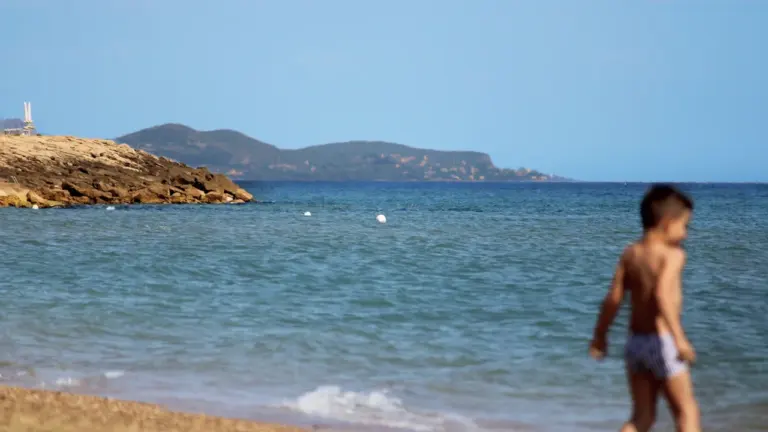 Un jeune garçon marche le long d'une plage ensoleillée en bord de mer.