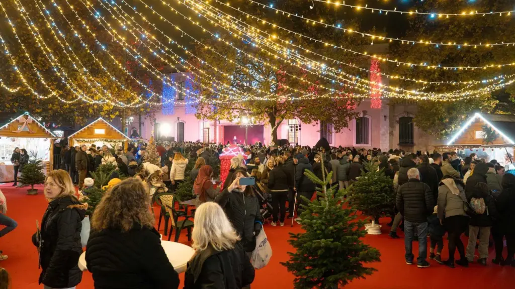 Une foule de personnes déambule sur un tapis rouge lors d'un marché de Noël nocturne.