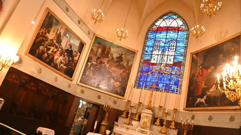 Intérieur d'église avec des peintures religieuses encadrées et un grand vitrail bleu lumineux.