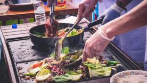 Mains en gants cuisinant des légumes frais sur une plancha pour un atelier culinaire.
