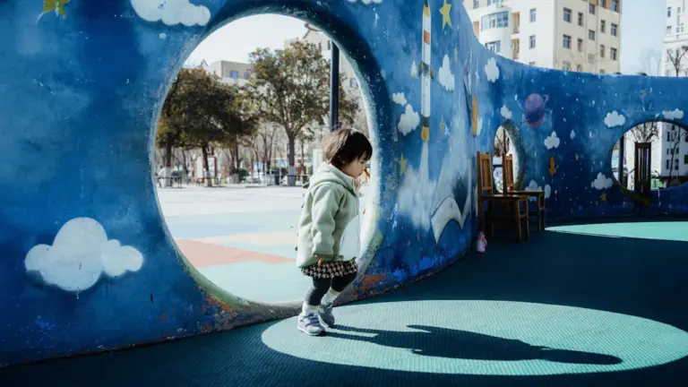 Une enfant joue dans un tunnel coloré sur une aire de jeux moderne.