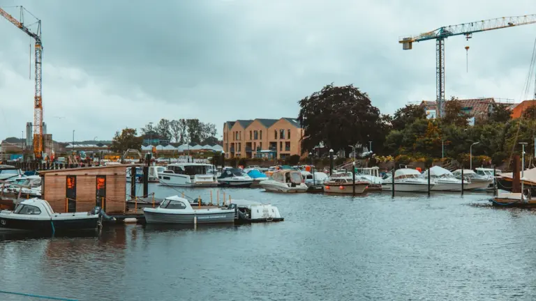 Bateaux amarrés dans un port de plaisance avec des bâtiments et des grues visibles.