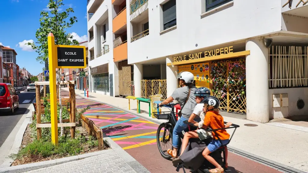 Une famille à vélo devant l'école Saint-Exupéry dans une rue apaisée et végétalisée.