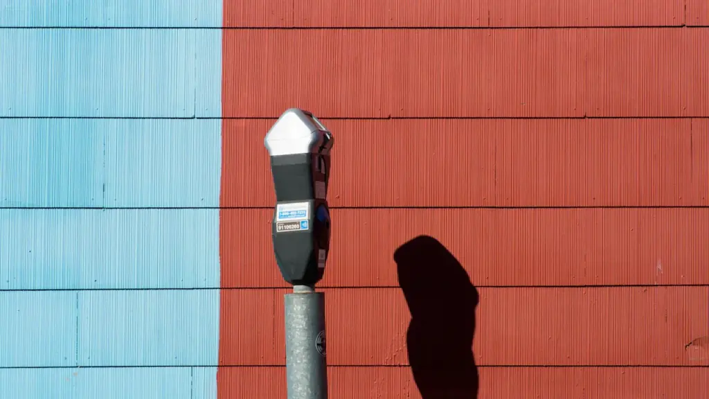 Un horodateur classique se dresse devant un mur bicolore rouge et bleu.