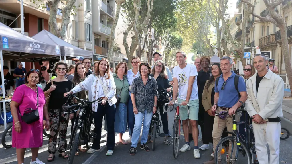 Un groupe de personnes souriantes pose avec leurs vélos dans une rue arborée en ville.